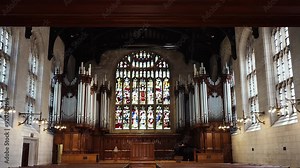Inside a cathedral or catholic church look at stained glass windows, pews, an organ, and pipes with beautiful sunlight shining through.