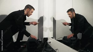 Mirror reflection: Man in black suit jacket fixes audio recording gear, reflected image
