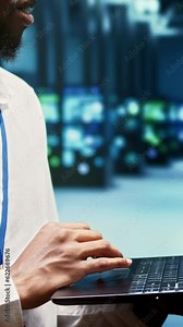 Vertical video Developer walking through mainframe rows delivering web content to online clients. Programmer in data center using laptop to make sure critical systems are in optimal condition, close