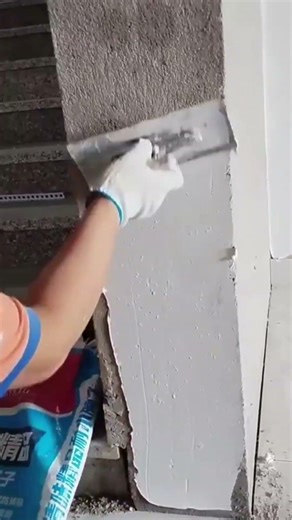 applying a smooth layer of wet white plaster onto a grey concrete pillar using a flat metal trowel