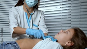 Pediatrician doctor examining a little girl by stethoscope. Doctor check lungs and listening to heartbeat of a girl kid in hospital bed