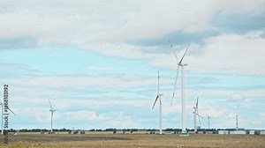 A small flock of birds fly over an agricultural field that has been ploughed. On horizon, wind turbine generating electricity. Slow motion. wide shot
