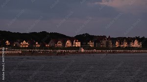 People enjoying the water on the beach of Warnemünde, Germany on a warm summer evening. Hotels and houses along the coast of the Baltic Sea in sunset lights with amazing reflections on their windows.