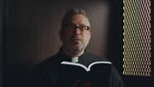 Catholic priest in cassock and glasses reading Holy Bible and praying...