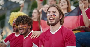 Group of muti-ethnic people clapping their hands and shouting something from tribunes. Friends cheering for national German team. Wearing wigs and facial pain symbolizing German flag.