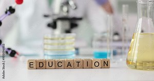 Word Education made of wooden cubes on laboratory table against flask of reagent, glass Petri dishes and microscope. Practical training in medical institution lab