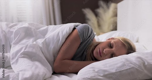 Woman sleeping. High angle view of beautiful young woman lying in bed and keeping eyes closed while covered with quilt.