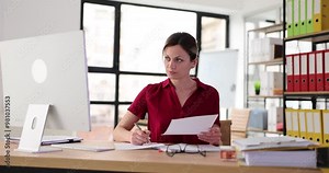 Woman manager sits at desk in office and works with documents on computer. Preparation of financial business report