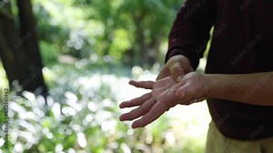 Elderly man stands and massages his palms and wrists, using his right hand to apply pressure points to relieve aches and pains from rheumatism.