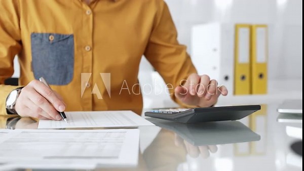 Professional calculating finances using a desktop calculator and writing on tax documents in an office setting. Audit and taxes in business