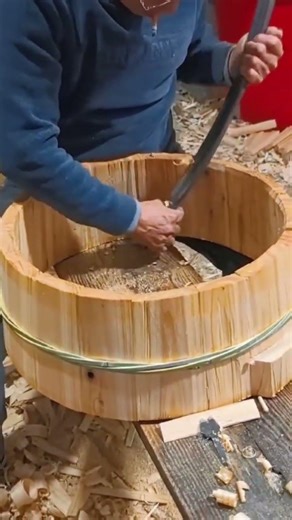 craftsman uses a curved planer tool to smooth the inner surface of large wooden container