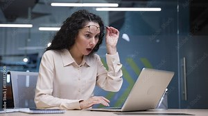 Surprised happy businesswoman looking at camera after reading great news on laptop sitting at a desk in business office. Excited shocked woman celebrating success, takes off glasses in surprise. Wow