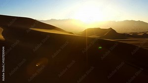 A high-speed FPV fly-through over desert dunes at sunrise with a distant mountain range.