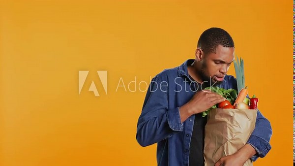Person counting all his freshly harvested produce in a paper bag, making sure he bought important ingredients for his vegan meals. Male model eating only ethically sourced food. Camera B.