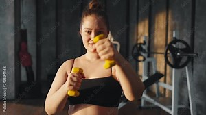 Woman doing exercises with dumbbells. Overweight young girl bodybuilder lifting dumbbell weights in gym, bicep curl exercise training. Sport female motivation, athlete training, lose weight concept.