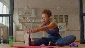 Determined active sporty fit black female practicing seated hamstring stretch exercise on fitness mat, strengthening spine and leg muscles, improving flexibility and posture while working out at home