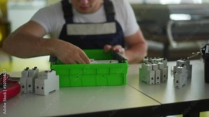 Electrician assembles electrical panel fuse box in workshop. Worker installs energy meter, switches and circuit breakers in distribution board on table.