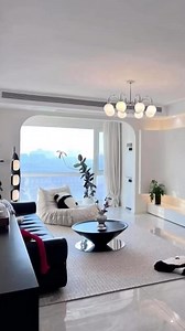 This living room is the definition of modern elegance and comfort. The glossy marble floors with bold veining instantly set a luxurious tone, reflecting the warm glow of the recessed LED lighting that runs seamlessly along the ceiling and built-in shelving. The lighting design not only adds depth but also creates a cozy, inviting atmosphere.A sleek black marble coffee table becomes the centerpiece, its polished surface contrasting beautifully with the soft neutral area rug beneath it. Surroundin