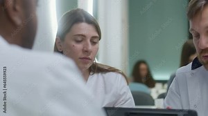 Adult doctor uses digital tablet computer, shows tests results to his colleagues. Female doctor looks at MRI or CT brain scan results on digital tablet. Medical staff have break in hospital cafe.
