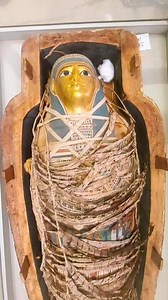 ✨ What secrets lie beneath this golden face—immortality wrapped in linen? ✨🪦☀️ This beautifully preserved mummy features a gilded mask, typical of the Late Period–Ptolemaic era, where gold symbolized purity and eternity, linking the deceased with Ra, the sun god. Beneath the linen wrappings lies a richly painted cartonnage, covered with protective deities, sacred symbols, and spells from the Book of the Dead, all meant to guide and protect the soul in the afterlife. Every layer reflects advance