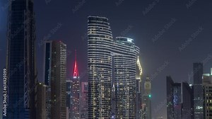 Futuristic towers and illuminated skyscrapers with lights in windows in Dubai Downtown and financial district. Urban city skyline aerial night timelapse. Dark sky