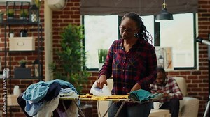 Frustrated housewife getting tired and angry about doing chores by herself, ironing laundry with steam and heat in apartment. Young adult being unhappy and stressed about housework.