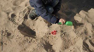 Little boy digging sand with shovel and playing on palyground at park. Concept of child development, sports and education.