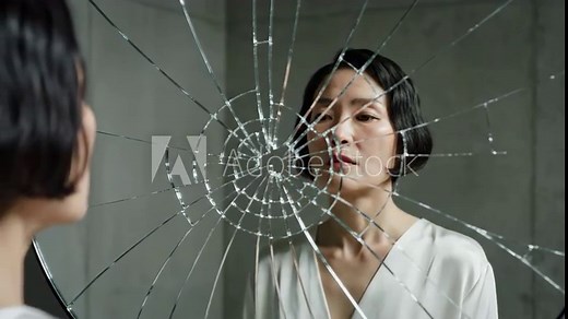 Cracked mirror with fragmented face reflection. A moody, minimal scene of a cracked mirror reflecting only broken fragments of a persons face.