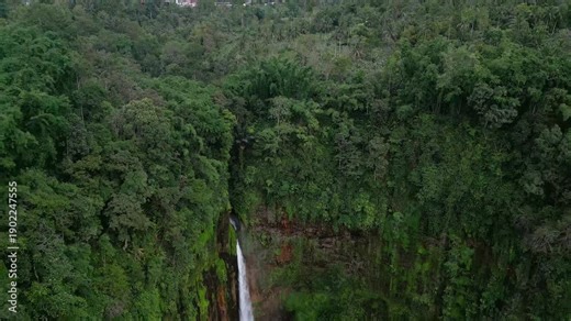 Drone video of a powerful waterfall crashing through dense jungle beneath Semeru Volcano. Dark volcanic cliffs, rising mist, and heavy water flow define this dramatic tropical landscape in East Java