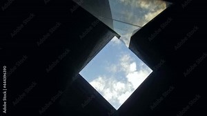 Low angle shot of camera rotating in square ceiling architecture detail. Blue sky background.