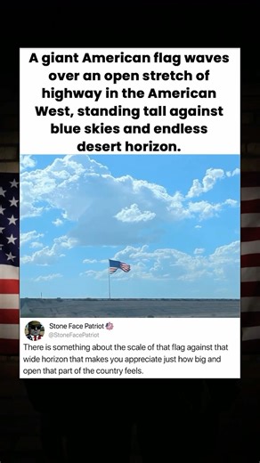 A giant American flag waves over an open stretch of highway in the American West, standing