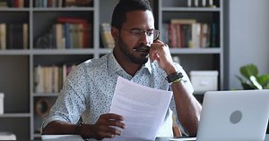 Serious focused african multiracial businessman student professional using laptop holding papers working sit at home office desk studying online doing research project preparing course work assignment