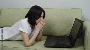 Angry upset young woman user customer using laptop feel frustrated mad about computer problem, worried reading bad news in social media lying down on couch at home.