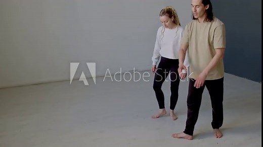 Young female dancer standing in fifth position, doing croise derriere and performing graceful arm move while learning ballet with male teacher during choreography lesson in studio