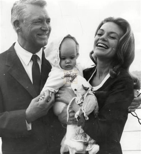 "Cary Grant and his fourth wife, Dyan Cannon, were photographed in 1966 aboard the S.S. Oriana with their baby daughter, Jennifer Grant, as they sailed to England. Grant, one of Hollywood’s most enduring leading men, was in his early sixties and radiated pride as a new father, while Cannon, a rising star of stage and screen, shone with youthful elegance and joy. Baby Jennifer, nestled in her parents’ arms, added sweetness to the family portrait. The photograph beautifully captures a rare glimpse