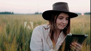 Farmer woman with tablet working in wheat field, she controls the harvesting process. The girl uses a tablet, plans to harvest. Concept of technology in agriculture. Smart farming technology.