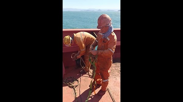 Seamen descend side of ship to remove cable tangled on anchor
