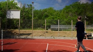 Side view of a happy blonde basketball player girl in a blue sports uniform warming up and hitting the ball off the floor during basketball training on a street sports ground in the summer