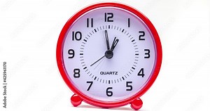 Small red alarm clock show the running time. A modern clock with red frame. Incessantly running time. Close up on a red plastic watch with second pointer on white background. Ten after twelve