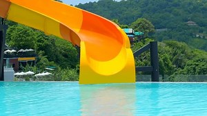 水着を着た女性がプールで滑り台を滑り降りる。女の子が楽しんで、ウォータースライダーを下る。夏休みに水遊び場で滑る。