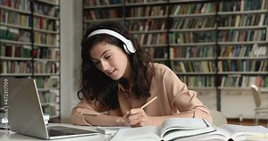 Student girl sit at desk in library takes notes in copybook talk to online tutor studying online use video call app on laptop. Video conference event, e-learn, generation Z, modern tech usage concept