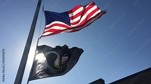 POW MIA flag flying along with American flag with sunlight illuminating through and a blue sky backdrop.