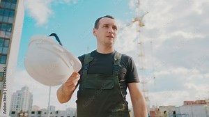 A worker work hard at construction site. Tired male builder wipes sweat from brow, standing in front of construction building. Heavy profession.Physical work in hot weather.