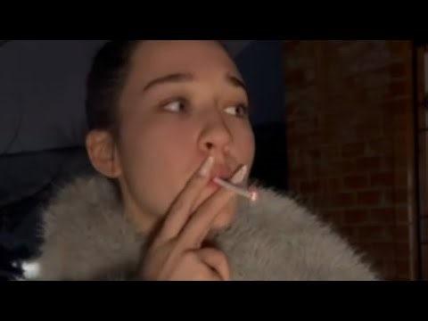 A beautiful girl smokes a cigarette in a fur coat and throws it away.