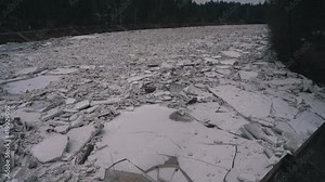 Huge Ice Loads Drift in the River Ogre, Latvia. Stedicam Shot in Snowy Mart Day. Congestion on the River in the Spring. A Large Cluster of Moving Ice Blocks