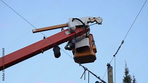 Low angle slow mo footage of powerline technician carrying out repairs from a cherry picker, as supplies are hoisted up to platform. With copy space.