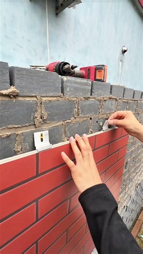 person is carefully installing a tile leveling clip onto a brick wall surface to ensure