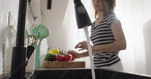Water flows from the tap while woman cooks in the kitchen. Water pours from water tap. Woman remembers to turn off running water. Wastewater, ecological problem Stock Video
