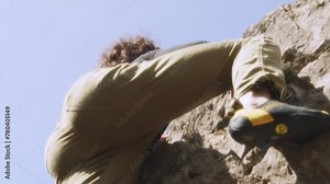 A climber, in careful motion, navigates a steep rock face in this cinematic slow-motion video. The wide-angle lens captures the vastness of the environment and the climbers interaction with the rugged