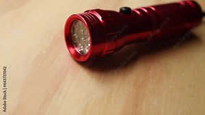 Red bright flashlight on a wooden table taken by a hand and being turned on